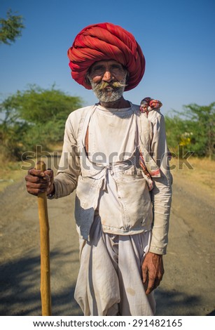 GODWAR REGION, INDIA - 14 FEBRUARY 2015: Elderly Rabari tribesman with big red turban and cane stands on road. Rabari or Rewari are an Indian community in the state of Gujarat.