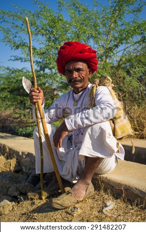 GODWAR REGION, INDIA - 14 FEBRUARY 2015: Elderly Rabari tribesman with red turban sits and holds ax and stick. Rabari or Rewari are an Indian community in the state of Gujarat.