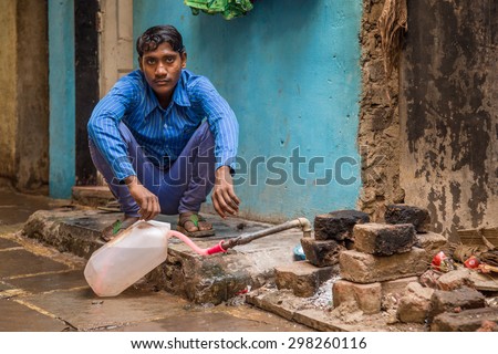 MUMBAI, INDIA - 12 JANUARY 2015: Young Indian man sits and fills water tank in street. Dharavi slum mostly has drinkable tape water in street but not in homes.