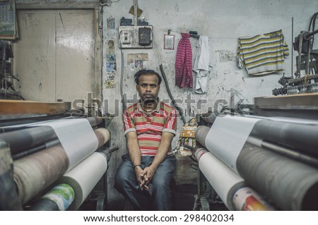 VARANASI, INDIA - 21 FEBRUARY 2015: Worker sits on chair next to textile machine in small factory. Post-processed with grain, texture and colour effect.