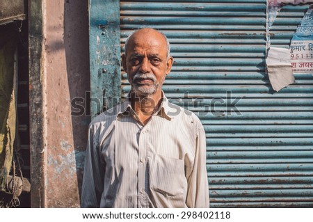 VARANASI, INDIA - 20 FEBRUARY 2015: Elderly Indian man with white beard stands in street next to closed store. Post-processed with grain, texture and colour effect.