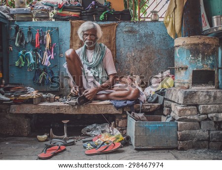 VARANASI, INDIA - 25 FEBRUARY 2015: Indian vendor sits in street shop and repairs slippers. Post-processed with grain, texture and colour effect.