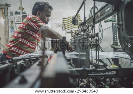 VARANASI, INDIA - 21 FEBRUARY 2015: Worker repairs textile machine in small factory. Post-processed with grain, texture and colour effect.