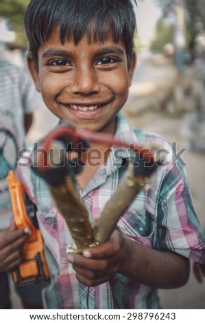 HAMPI, INDIA - 31 JANUARY 2015: Indian boy holds slingshot and toy truck. Post-processed with grain, texture and colour effect.