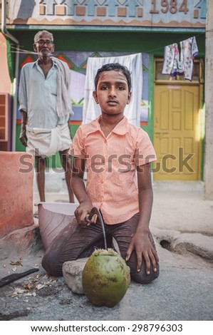 KAMALAPURAM, INDIA - 02 FABRUARY 2015: Indian boy opening a coconut in-front of house in a town close to Hampi. Post-processed with grain, texture and colour effect.
