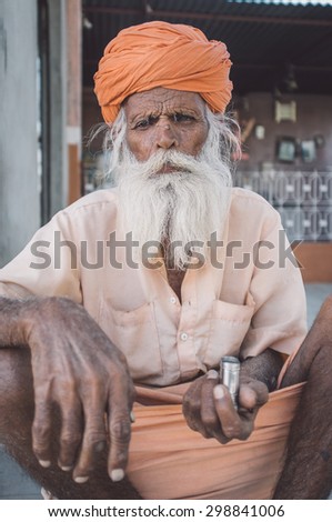 GODWAR, INDIA - 12 FEBRUARY 2015: Elderly Indian tribesman with turban in lungi sits on ground in front of temple. Post-processed with grain, texture and colour effect.