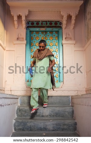 JODHPUR, INDIA - 07 FEBRUARY 2015: Woman in traditional clothes and scarf walking down stairs. Stone entrance and wooden door with gold panels are decorated in style typical to Rajasthan region.