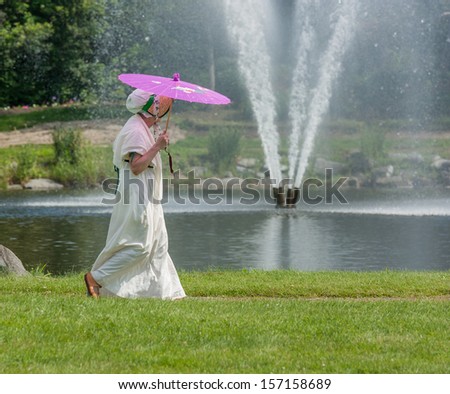 MORRISBURG, CANADA - JULY 14: A woman in period costume walks past a water fountain during the Battle of Crysler\'s Farm reenactment on July 14, 2013 near Morrisburg, Ontario.