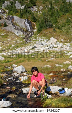 Filipino woman washing dishes in mountain stream while backpacking. British Columbia. Canada.