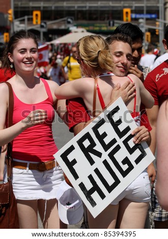 OTTAWA, CANADA – JULY 1: A young man with a \'Free Hugs\' sign embraces a stranger, while her friend looks on, during Canada Day festivities on July 1, 2011 in downtown Ottawa, Ontario.