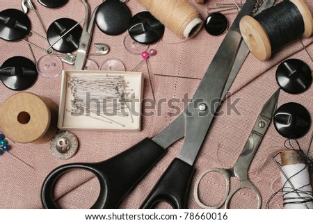 Sewing kit. Tailoring tools. Scissors, bobbins with thread, buttons and needles on the pink threaded fabric.