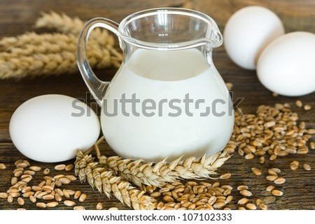 Glass jug with milk, wheat seeds and eggs