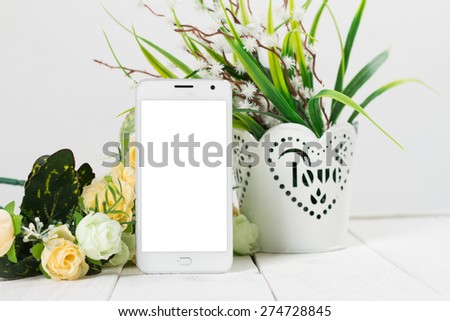 White mobile phone with a blank screen in the flower arrangement on the table