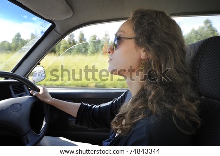 profile of a pretty young woman in sunglasses driving a right-hand drive vehicle