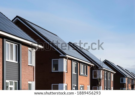 Solar panels mounted on the roofs of a row modern new-build houses in a street in Lemmer, Friesland, the Netherlands with sun and blue sky. Sustainable energy