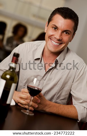 Handsome young man with a glass of wine smiling at camera in a restaurant