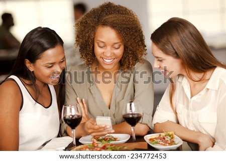 Group of mixed-race girls looking at a smartphone in a restaurant.