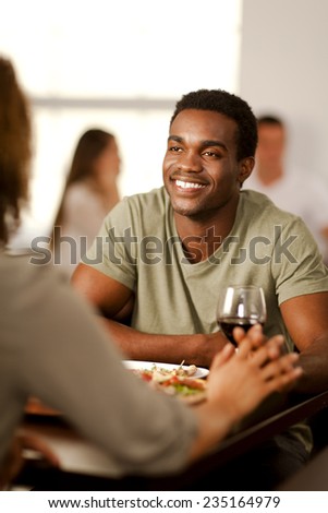 Handsome young African-American man holding hands with his girlfriend in a restaurant.