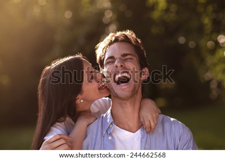 Beautiful young woman affectionately biting her boyfriend\'s ear in a park