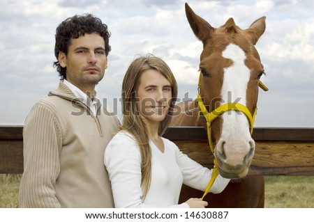 A young couple posing with their horse at the stable