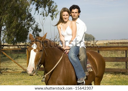 A young couple riding their horse on a rural farm on a cloudy day