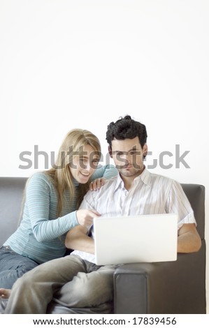A young couple at home on the sofa excited about what they\'re seeing on their laptop computer