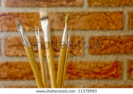 artist painting brushes in front of a bricks wall