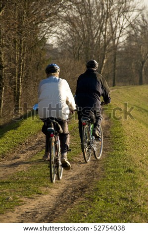 couple of elder people riding in bicycle along a path on the riverbank