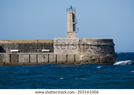 Old small stone lighthouse over blue sky and ocean