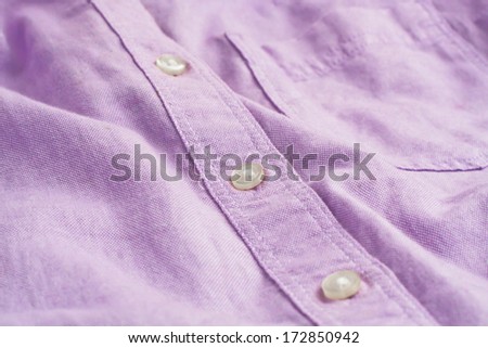 Close up of a button on a plain lilac women\'s shirt with shallow depth of field