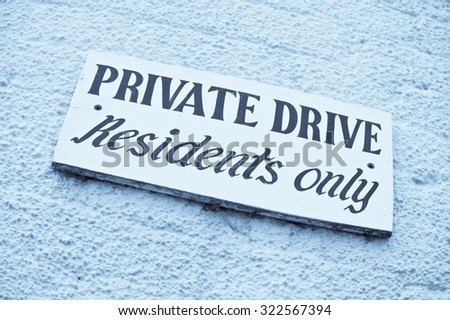 A sign for a private drive on a brick wall, in blue monochrome