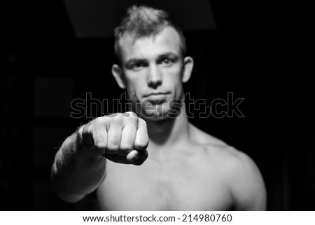 Male fitness model showing muscles in studio with a black background