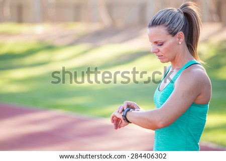 Fit female athlete looking at her watch with a heart rate monitor built in to track her progress of her exercise on a tartan athletics track.