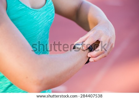Fit female athlete looking at her watch with heart rate monitor built in to track her progress of her exercise on a tartan athletics track.