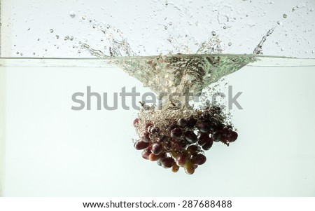 Fresh bunch of red grapes splashing into water on a white background.