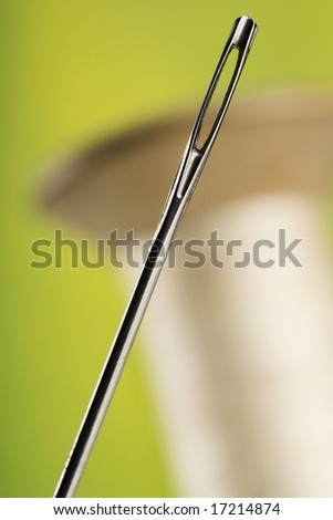 needle and the spool of thread against green-yellow background (focus on the needle)