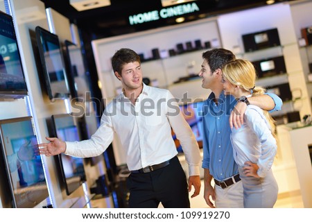 A couple looking at television screens for sale while being assisted by a store clerk