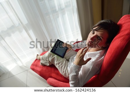 Young woman at home relaxing in her lliving room reading a digital tablet PC surf internet and work