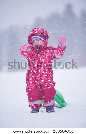 happy family on winter vacation, mom and cute little girl have fun and slide while snow falkes falling