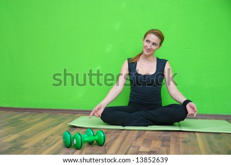 pretty girl practicing yoga in fitness club with green wall in background