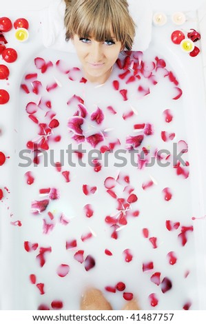 woman beauty spa and wellness treatment with red flower petals in bath with milk