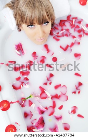 woman beauty spa and wellness treathment with red flower petals in bath with milk
