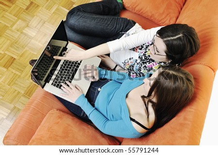 two happy young woman working on laptop computer on red sofa isolated on white
