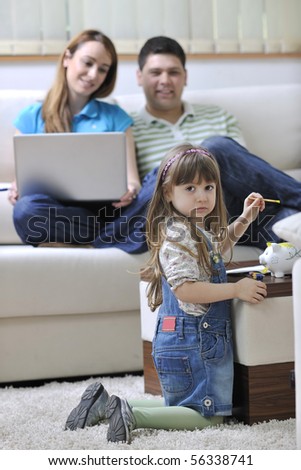 young happy family at bright and modern living room putting money in piggy bank and working on laptop computer on home finance