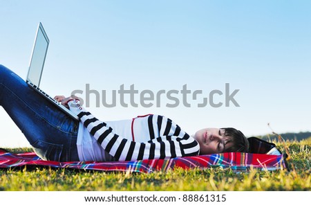 young teen woman work on laptop computer outdoor in nature with blue sky and green grass in background