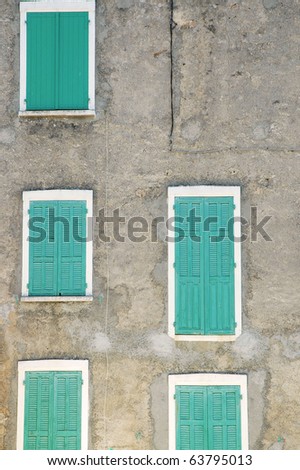 Closed green window shutters on a gray house facade.