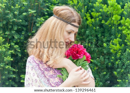 Woman in profile with red hair, dressed as a hippie, with a bouquet of peonies in the park.