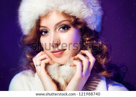 Portrait of beautiful girl with winter fur cap on purple background