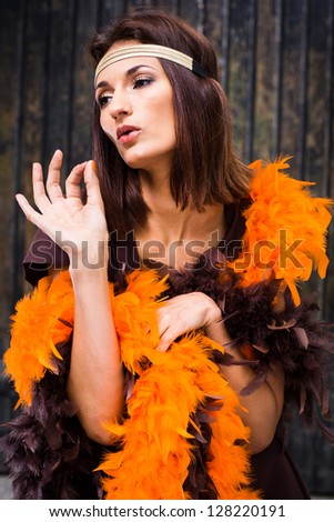 beautiful actress in brown and orange boa posing against old wooden gate