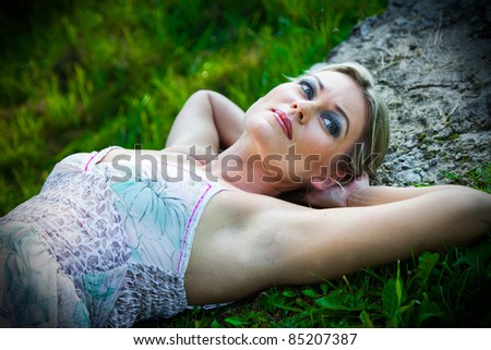 Portrait of attractive woman in blue sundress lying on stones against natural landscape at summer morning